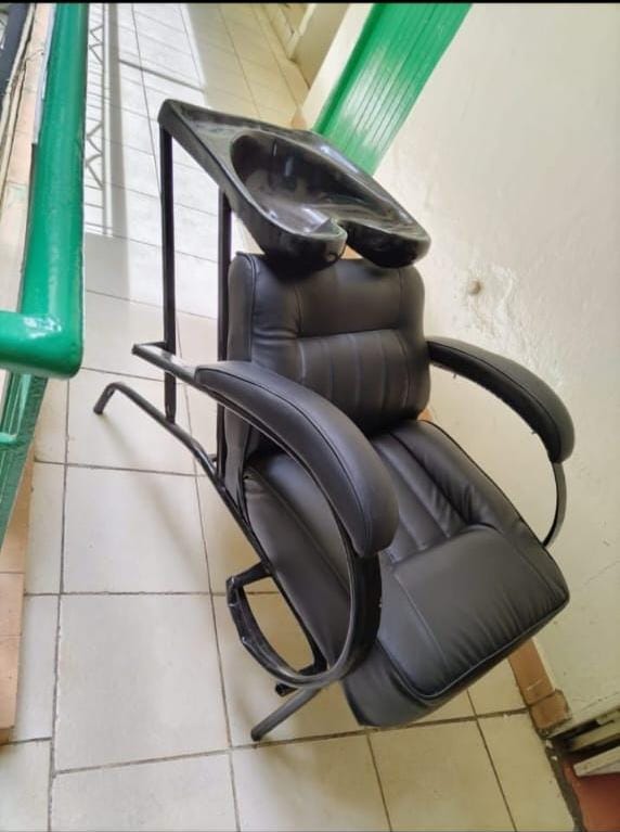 Barber chair with an integrated sink. The chair features a thickly padded seat and backrest for client comfort. It is constructed with a sturdy metal frame and premium leatherette upholstery.