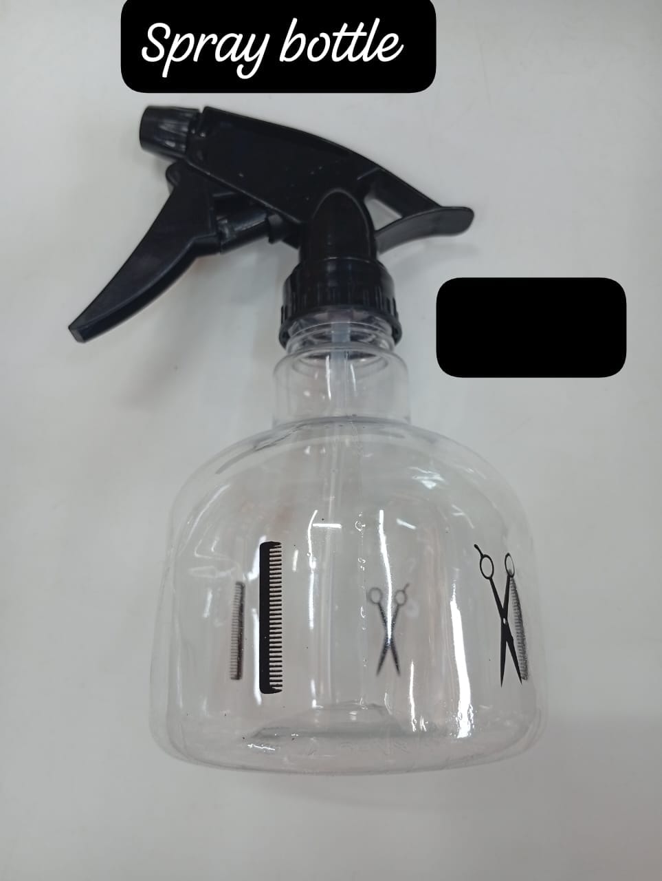 This is a clear plastic hairdressing water spray bottle with black accents. 
Features a trigger-operated spray mechanism.
Includes graphics of hairdressing tools (comb and scissors) on the side.
Avail