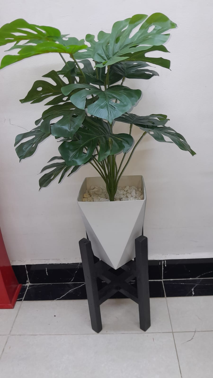 Artificial plant, plastic vase with white decorative pebble stones and a wooden stand