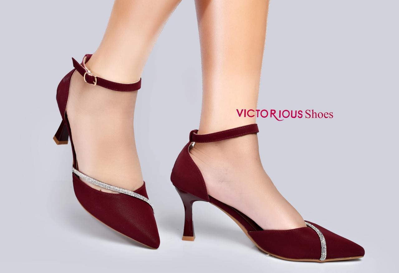 Elegant black pointed-toe kitten heels by Victorious Shoes. They feature a chic ankle strap with a delicate buckle, a subtle cut out, and a stunning curved rhinestone accent across the toe.