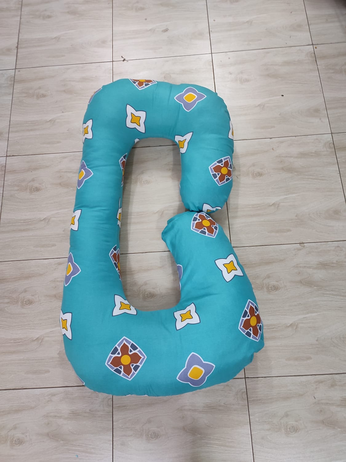 G-shaped maternity and pregnancy support pillow support pillow resting vertically on a light-colored tiled floor.Key Visual Details:Shape: It features