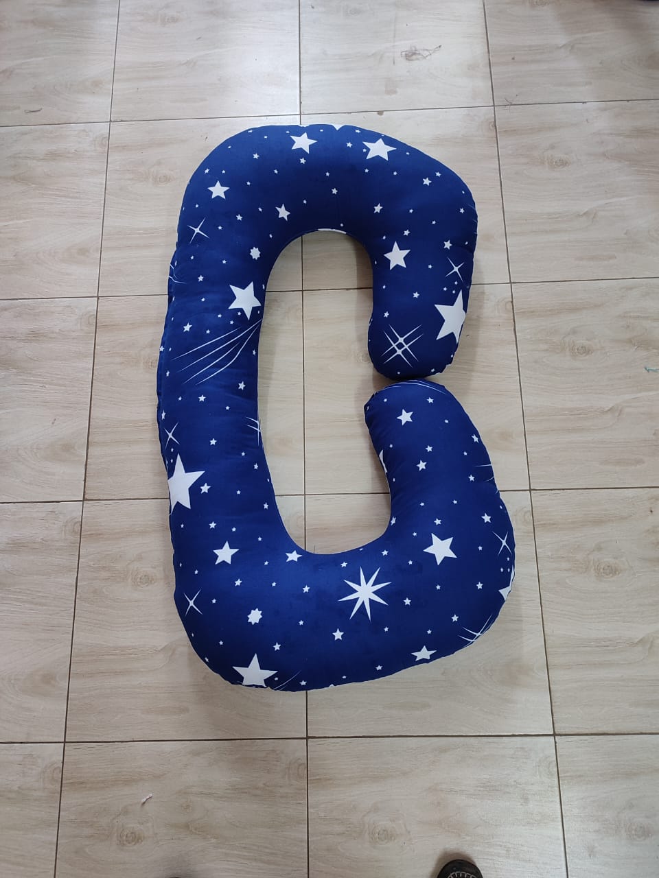 G-shaped maternity and pregnancy support pillow support pillow resting vertically on a light-colored tiled floor.Key Visual Details:Shape: It features