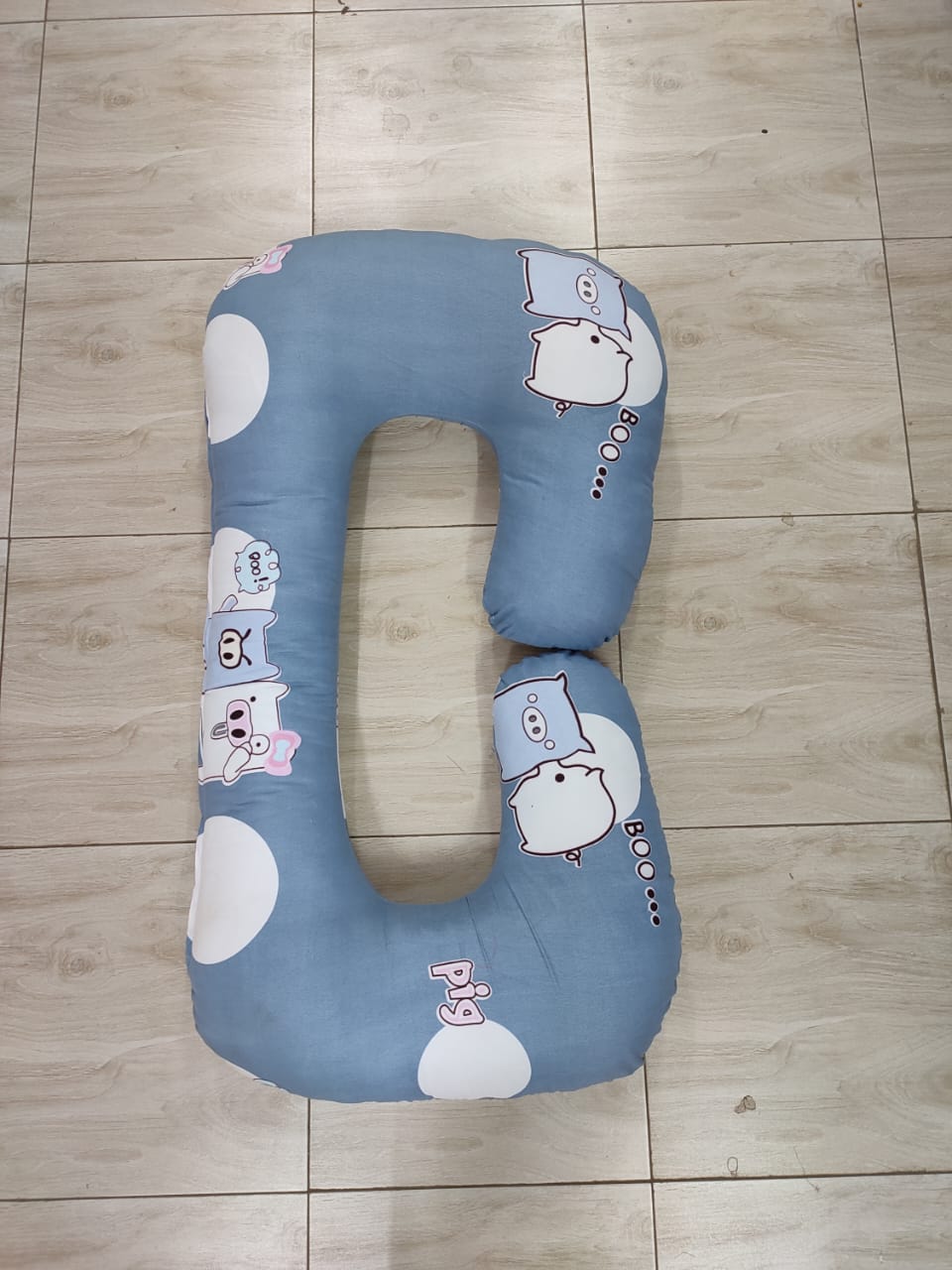 G-shaped maternity and pregnancy support pillow support pillow resting vertically on a light-colored tiled floor.Key Visual Details:Shape: It features